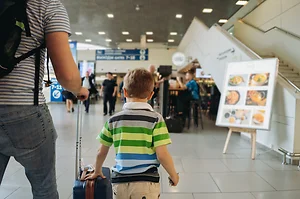 Father and cute boy in airport with backpack and suitcase. Travelling with kids